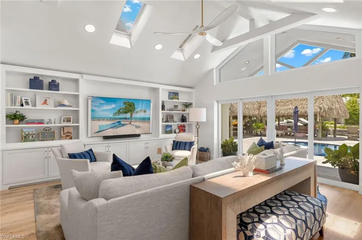 Living room with light wood-type flooring, built in shelves, high vaulted ceiling, ceiling fan, and a skylight