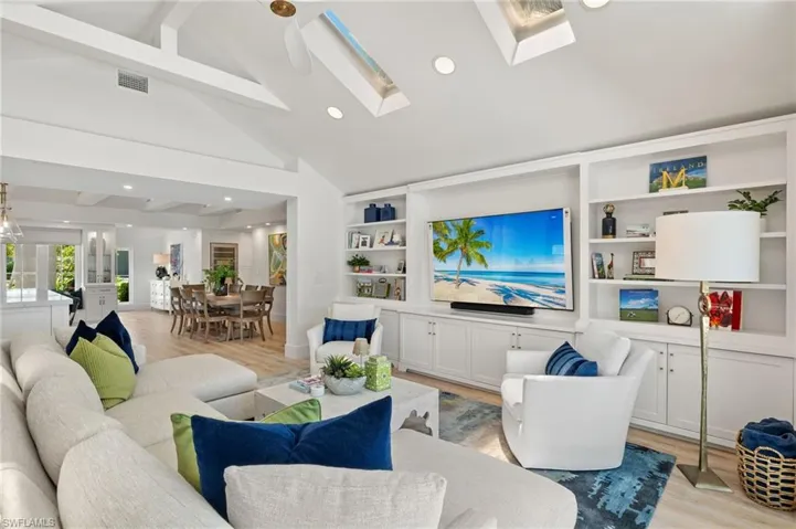 Living room featuring high vaulted ceiling, built in features, light wood-type flooring, and a skylight
