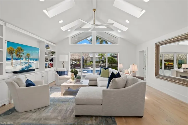 Living room with high vaulted ceiling, built in features, a skylight, and light hardwood / wood-style flooring