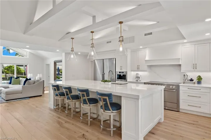 Kitchen with light hardwood / wood-style floors, a center island with sink, high end appliances, premium range hood, and pendant lighting