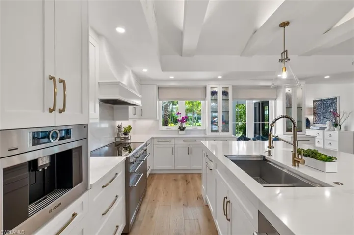Kitchen with custom range hood, light wood-type flooring, high end range oven, white cabinets, and sink