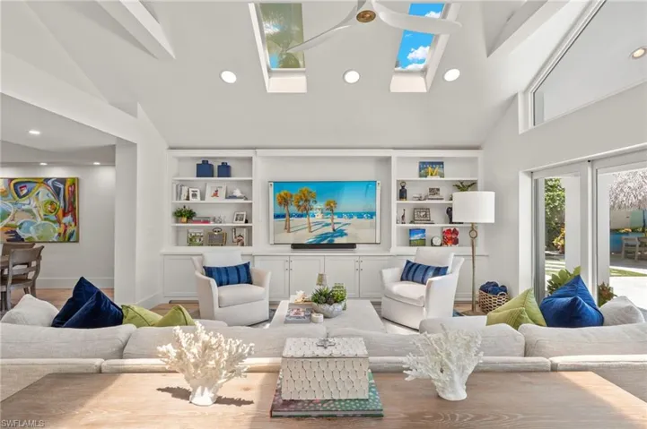 Living room featuring high vaulted ceiling, ceiling fan, built in features, and a skylight