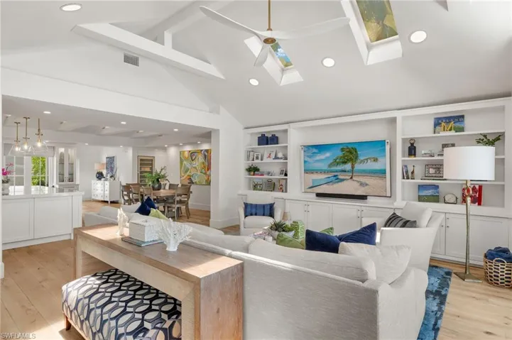 Living room with ceiling fan, light hardwood / wood-style flooring, built in shelves, high vaulted ceiling, and a skylight