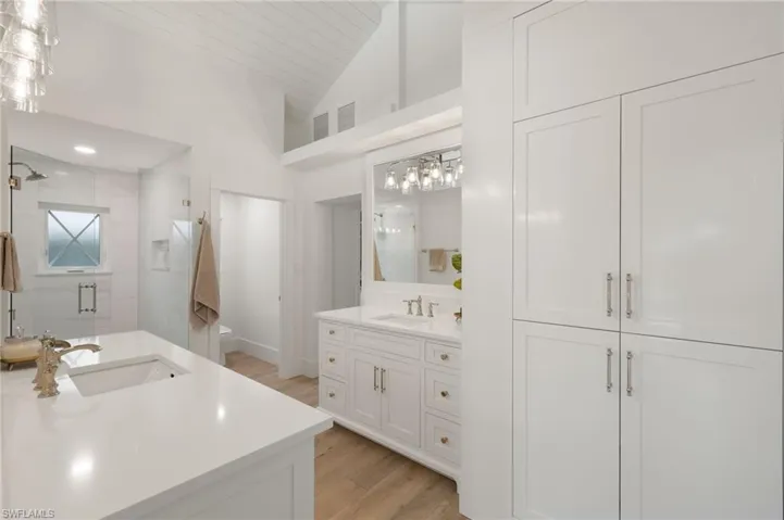 Bathroom featuring high vaulted ceiling, hardwood / wood-style flooring, large vanity, and dual sinks
