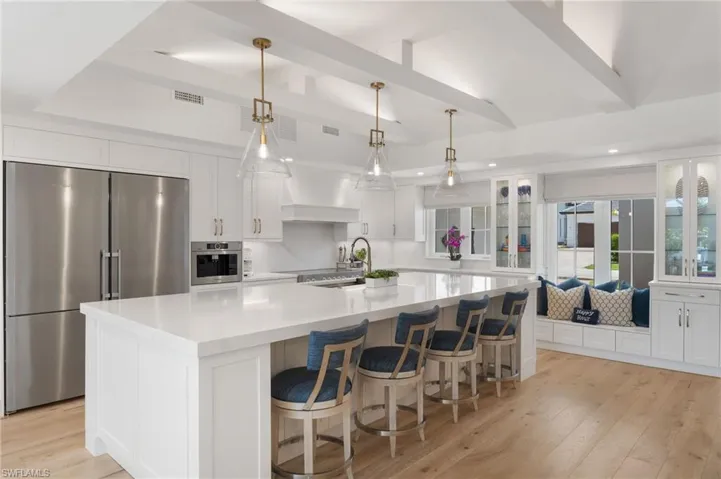 Kitchen with decorative light fixtures, light hardwood / wood-style floors, stainless steel appliances, white cabinetry, and an island with sink