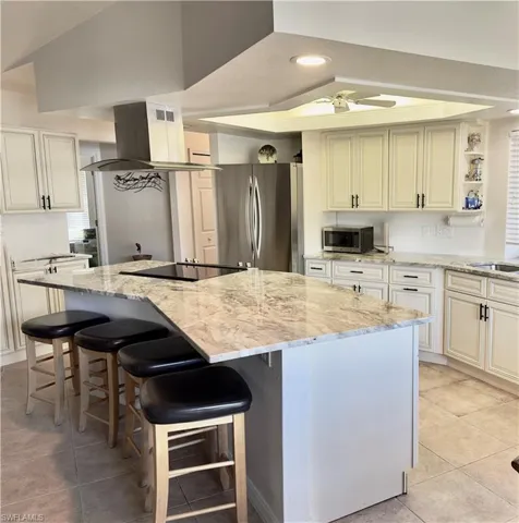 Kitchen featuring light tile patterned floors, a center island, island exhaust hood, appliances with stainless steel finishes, and light stone countertops