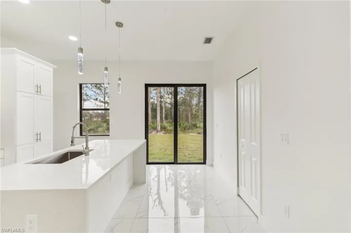 Kitchen with pendant lighting, white cabinetry, a kitchen island with sink, and sink