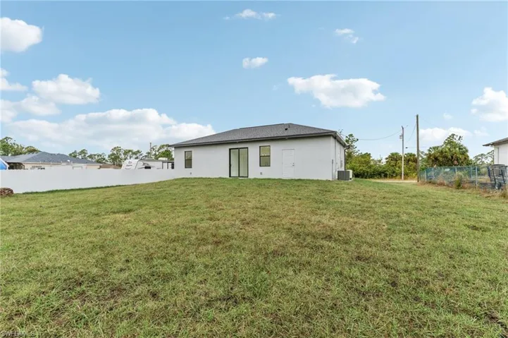 Back of house with central AC unit and a lawn