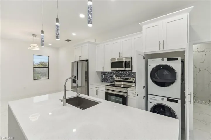 Kitchen featuring stacked washer and clothes dryer, sink, appliances with stainless steel finishes, decorative light fixtures, and white cabinetry
