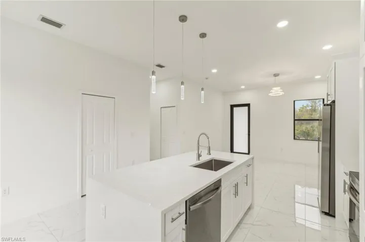 Kitchen with white cabinetry, a kitchen island with sink, hanging light fixtures, and stainless steel appliances