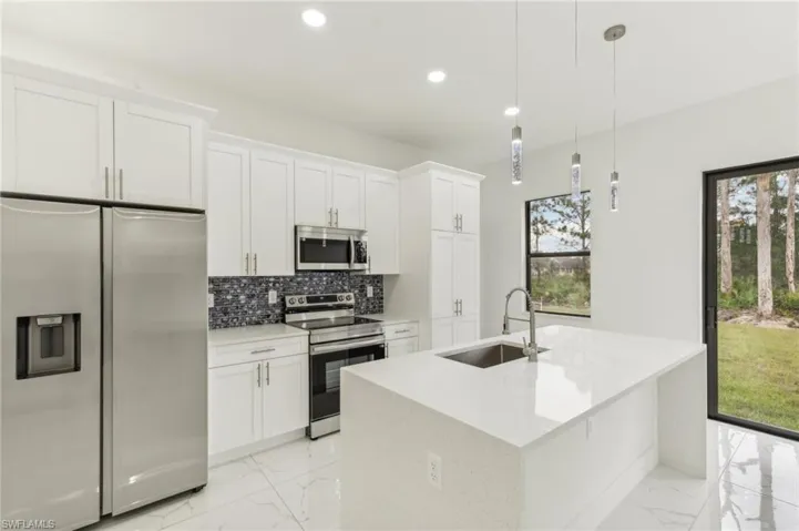 Kitchen with white cabinets, decorative light fixtures, sink, and stainless steel appliances