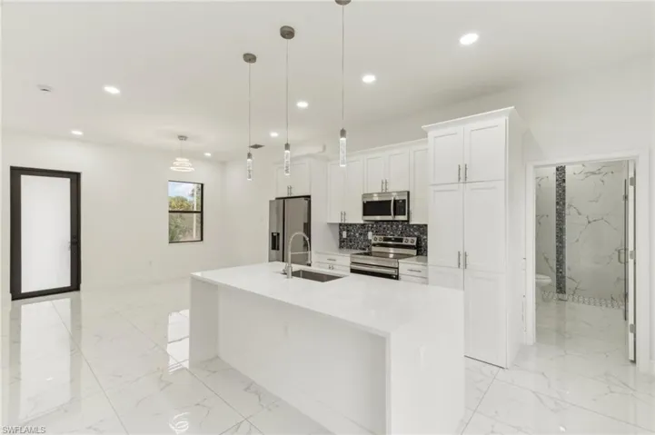 Kitchen with sink, stainless steel appliances, decorative light fixtures, a center island with sink, and white cabinets