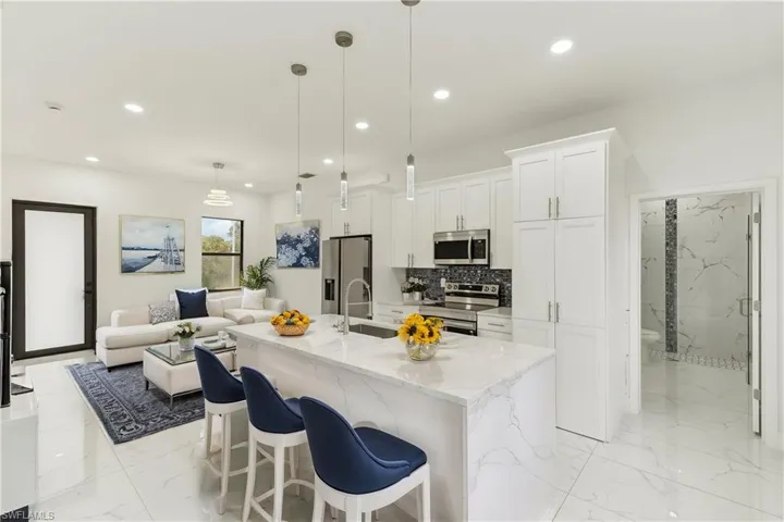 Kitchen featuring light stone countertops, hanging light fixtures, a center island with sink, white cabinets, and appliances with stainless steel finishes