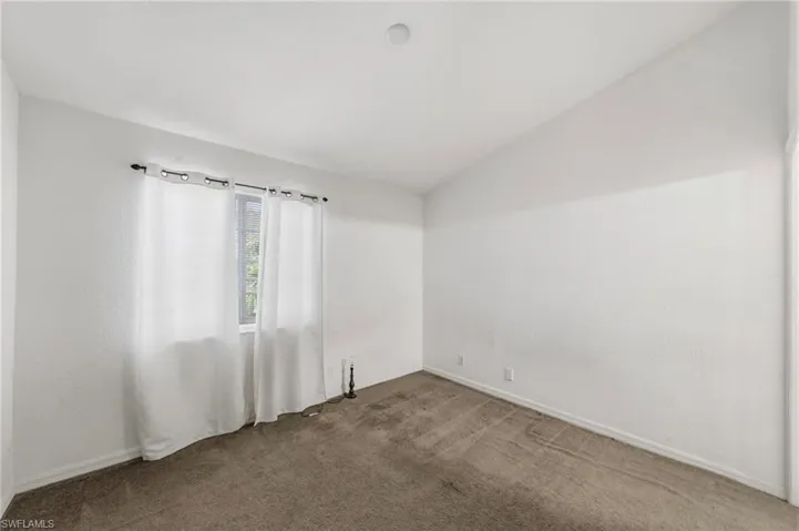 Unfurnished room featuring lofted ceiling and dark carpet