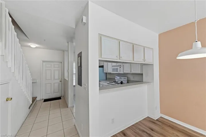 Kitchen with white appliances, white cabinetry, hanging light fixtures, light countertops, and light wood finished floors