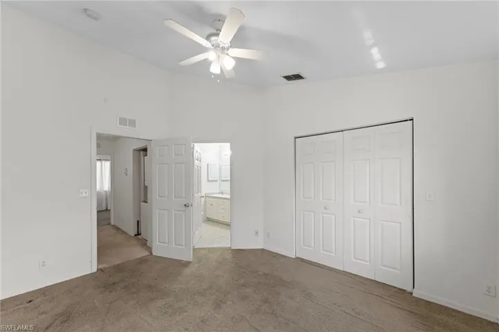 Unfurnished bedroom with carpet, a closet, a ceiling fan, ensuite bathroom, and lofted ceiling
