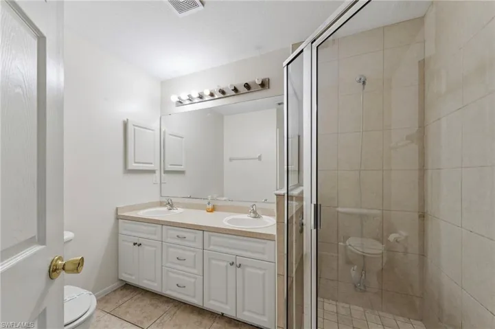 Full bath with double vanity, a stall shower, and light tile patterned floors