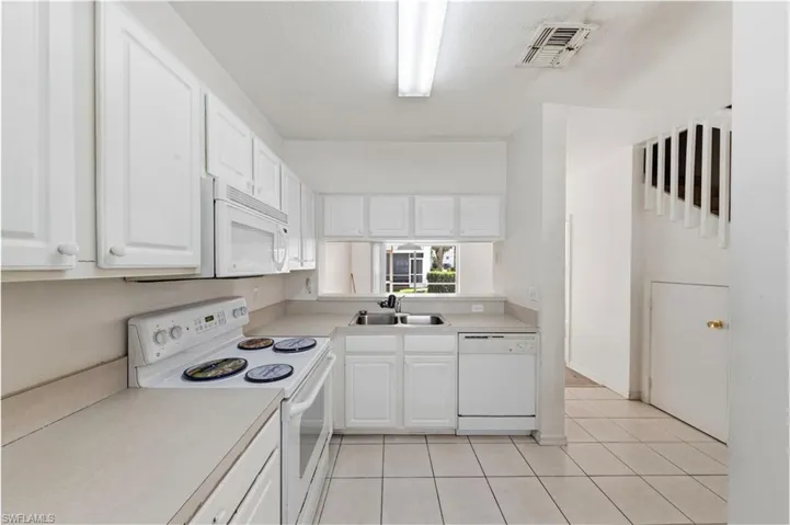 Kitchen with white appliances, light countertops, white cabinets, and light tile patterned floors