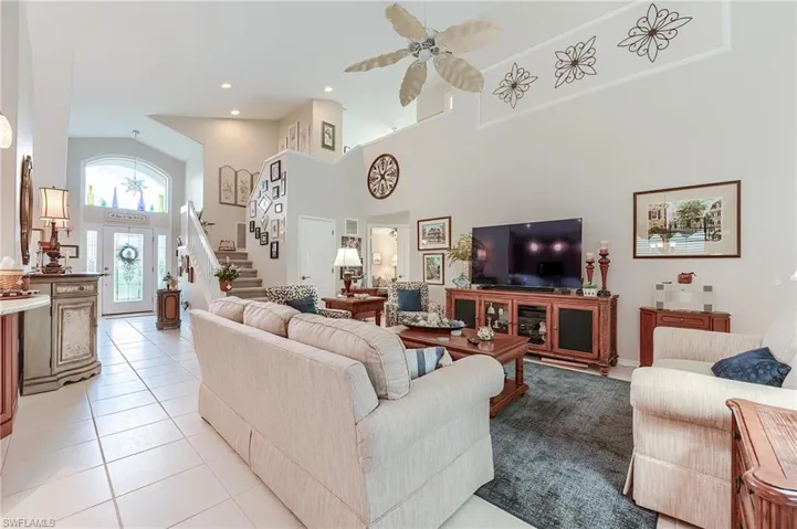 Living room featuring light tile patterned floors, ceiling fan, recessed lighting, stairway, and a high ceiling