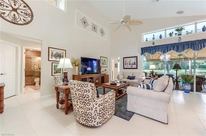 Tiled living room with a towering ceiling, visible vents, baseboards, and a ceiling fan