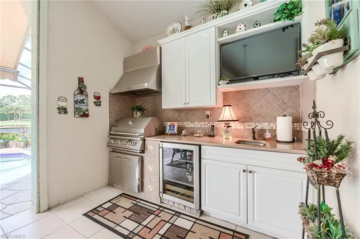 Kitchen featuring decorative backsplash, wine cooler, a sink, and wall chimney exhaust hood