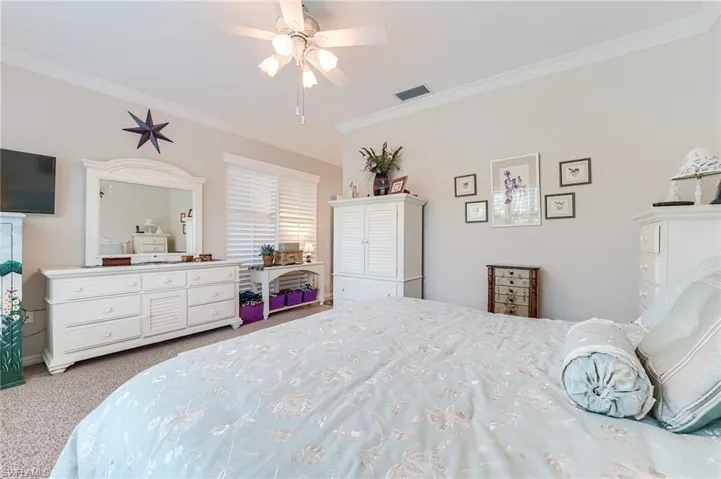 Carpeted bedroom with visible vents, baseboards, ornamental molding, and ceiling fan