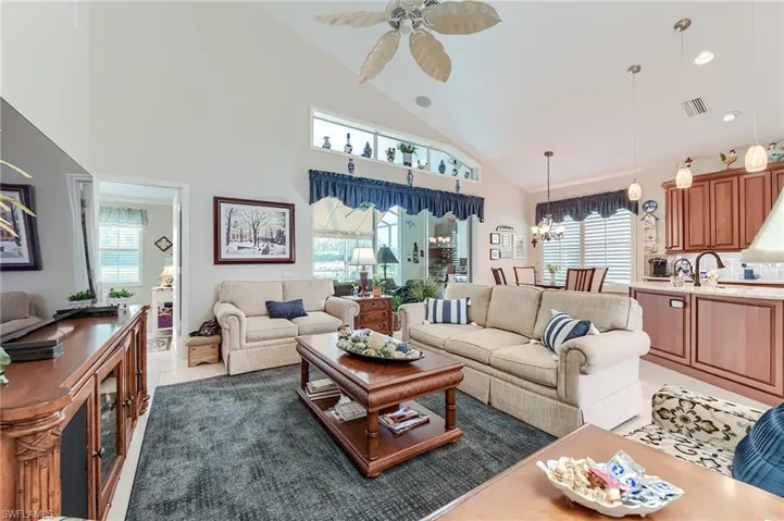 Living area with ceiling fan with notable chandelier, light tile patterned floors, visible vents, and plenty of natural light