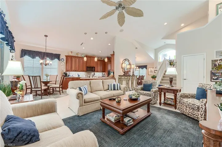 Living room featuring ceiling fan with notable chandelier, high vaulted ceiling, recessed lighting, and stairway