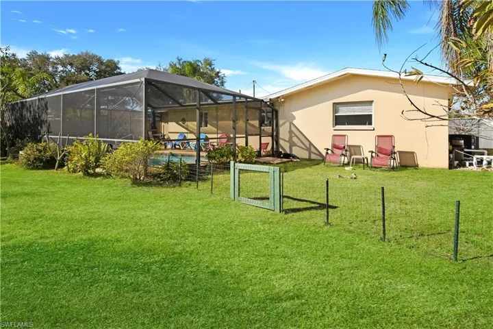 Back of house featuring a lanai, a yard, stucco siding, and an outdoor pool