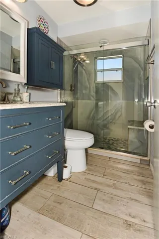 Full bathroom featuring vanity, a marble finish shower, and wood finish floors