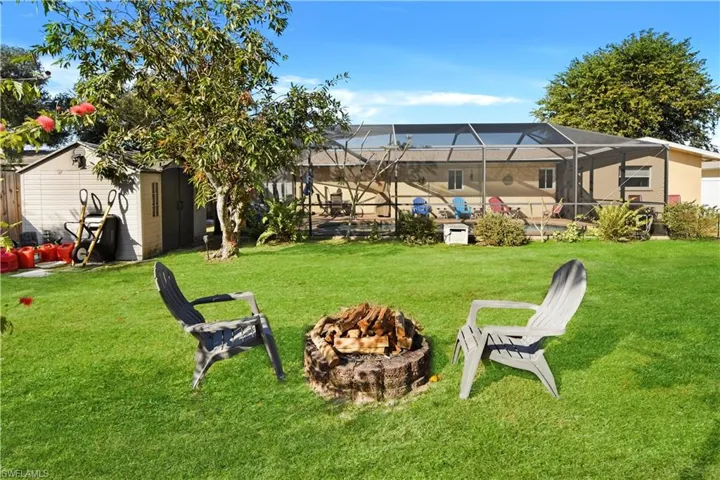 View of green lawn with a sunroom, a fire pit, a lanai, a swimming pool, and a storage shed