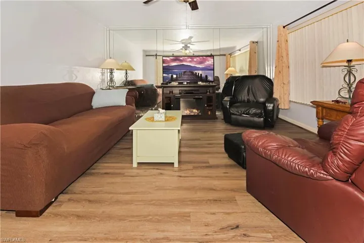 Living area with light wood-style flooring, a ceiling fan, and a warm lit fireplace