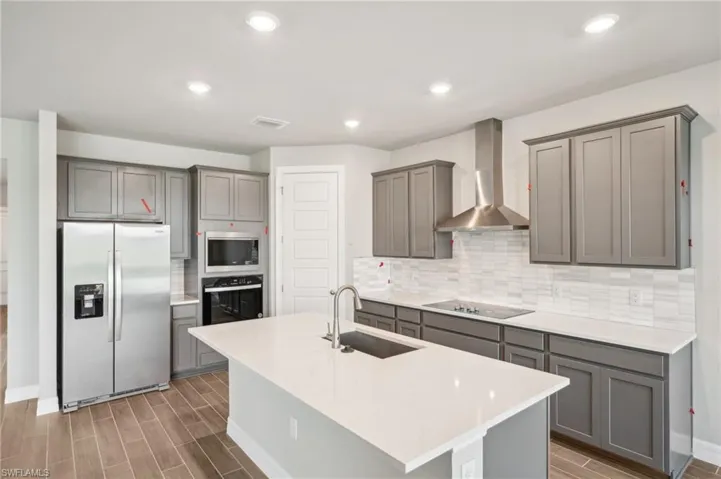 Kitchen featuring black appliances, a sink, wall chimney exhaust hood, gray cabinetry, and recessed lighting