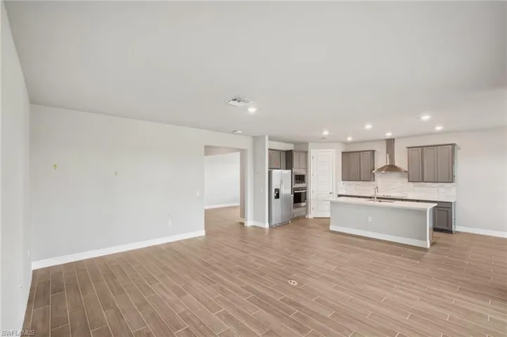 Unfurnished living room featuring baseboards, a sink, light wood-type flooring, and recessed lighting