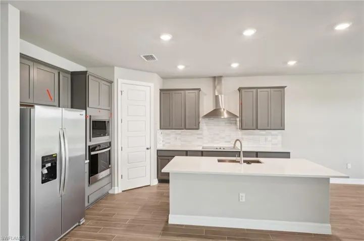 Kitchen featuring stainless steel appliances, wall chimney exhaust hood, a sink, light wood-style floors, and recessed lighting