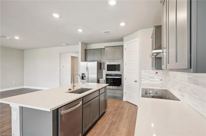 Kitchen with a sink, stainless steel appliances, gray cabinetry, light wood-style floors, and light countertops