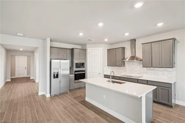 Kitchen with stainless steel appliances, wall chimney exhaust hood, gray cabinetry, light wood-style flooring, and recessed lighting