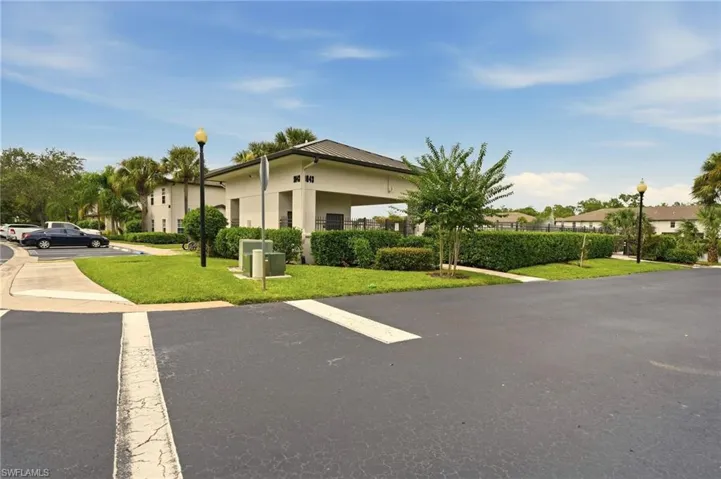 Paved parking area, lush green landscaping, mature palm trees, and a covered building entrance