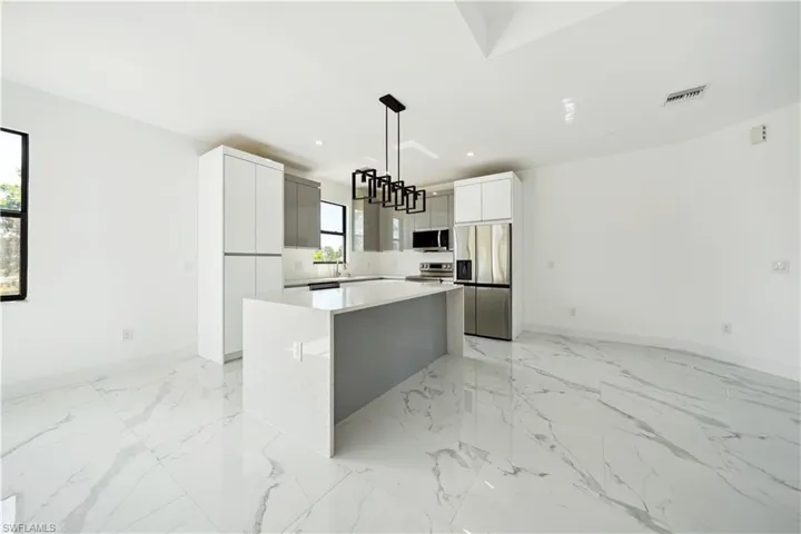 Kitchen featuring appliances with stainless steel finishes, a center island, white cabinets, light marble finish floors, and recessed lighting