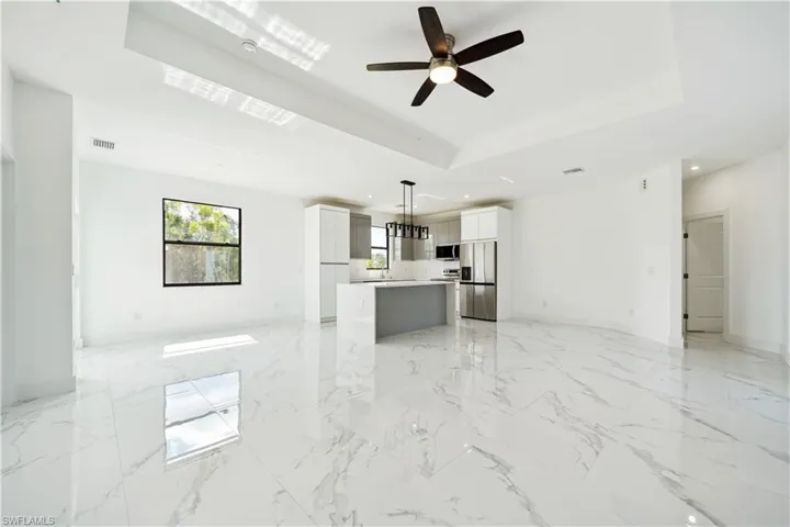 Kitchen featuring open floor plan, stainless steel appliances, a tray ceiling, light marble finish flooring, and light countertops