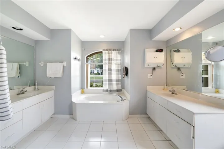 Bathroom with baseboards, two vanities, a garden tub, and recessed lighting