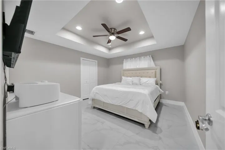 Tray ceiling with recessed lighting and a ceiling fan, light gray wall paint, white bi-fold closet doors, and marble-look tile flooring