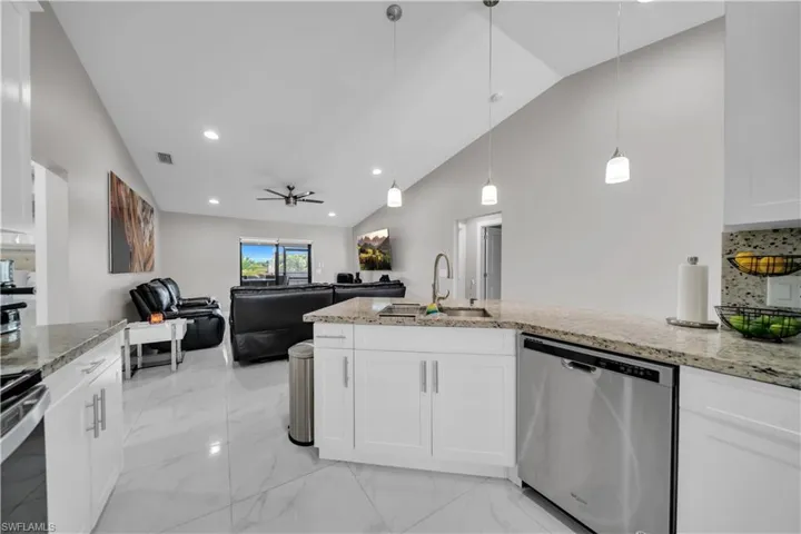Open-concept kitchen and living area featuring vaulted ceilings, white shaker-style cabinetry, granite countertops, and stainless steel appliances