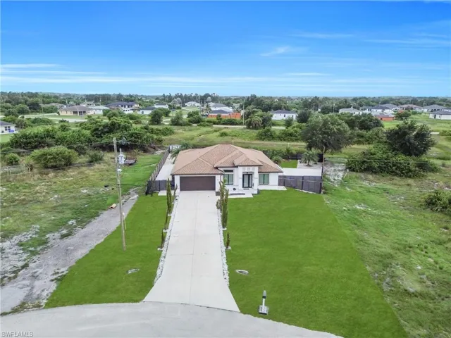 Contemporary stucco exterior with a tiled hip roof, featuring an attached garage, a long concrete driveway, and a front lawn with established landscaping