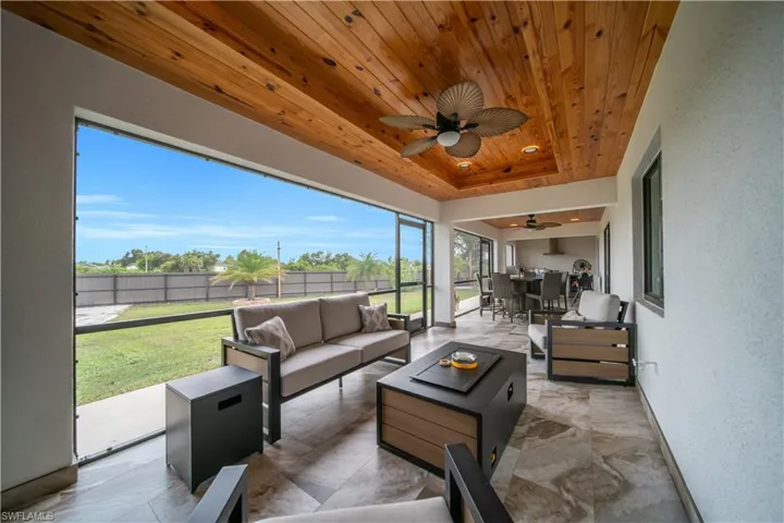 Screened outdoor living area featuring a wood-panel ceiling, ceiling fan, and large format floor tiles
