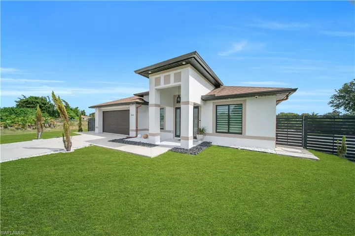 Modern exterior architecture with a prominent front entrance, a two-car garage with an automatic door, a gravel landscape bed, and a privacy fence
