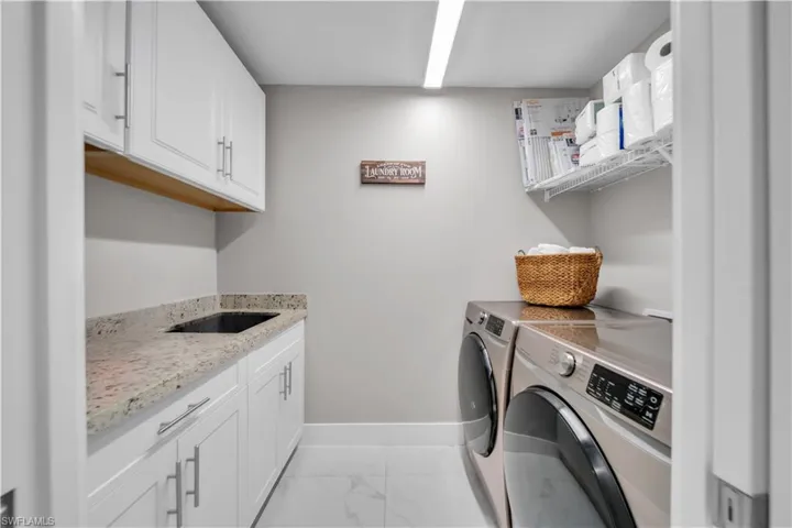 Dedicated utility space featuring white cabinetry, light-toned countertop with an integrated sink, and white tiled flooring