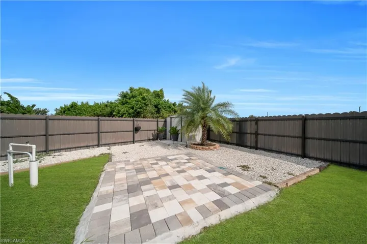 Expansive backyard featuring a paver patio area, gravel landscaping, and a mature palm tree