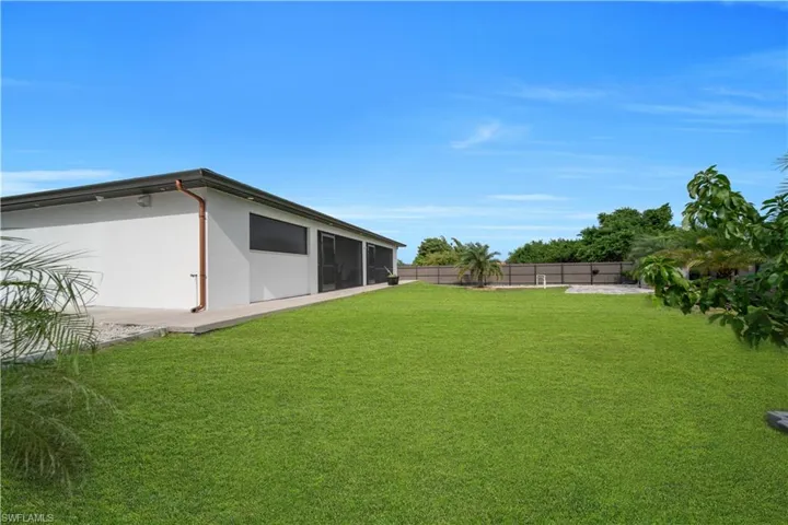 Expansive grassy lawn with a concrete patio and a modern exterior building featuring screened doors and windows