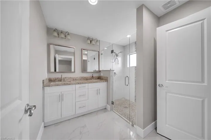 Bathroom with a glass-enclosed shower, dual vanity with light-toned countertops, and white cabinetry